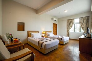 Ein Hotelzimmer mit zwei Betten, Holzboden, Schreibtisch mit Wasserkocher und einem Vorhangfenster.