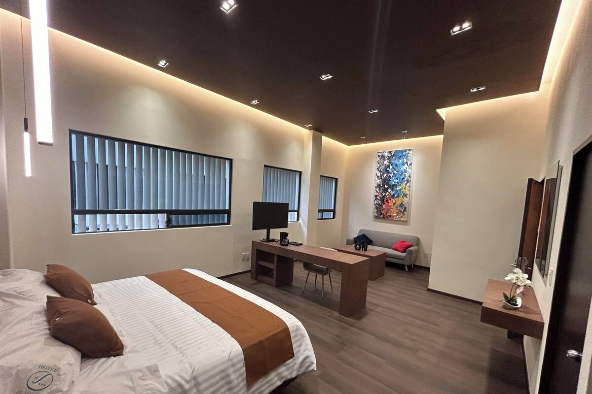 Une chambre d’hôtel moderne dotée d’un grand lit, d’un bureau, d’un canapé et d’une grande fenêtre avec des stores.