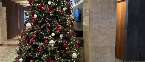A large Christmas tree with red and white ornaments, surrounded by gift boxes, in a lobby with marble flooring and a modern design.