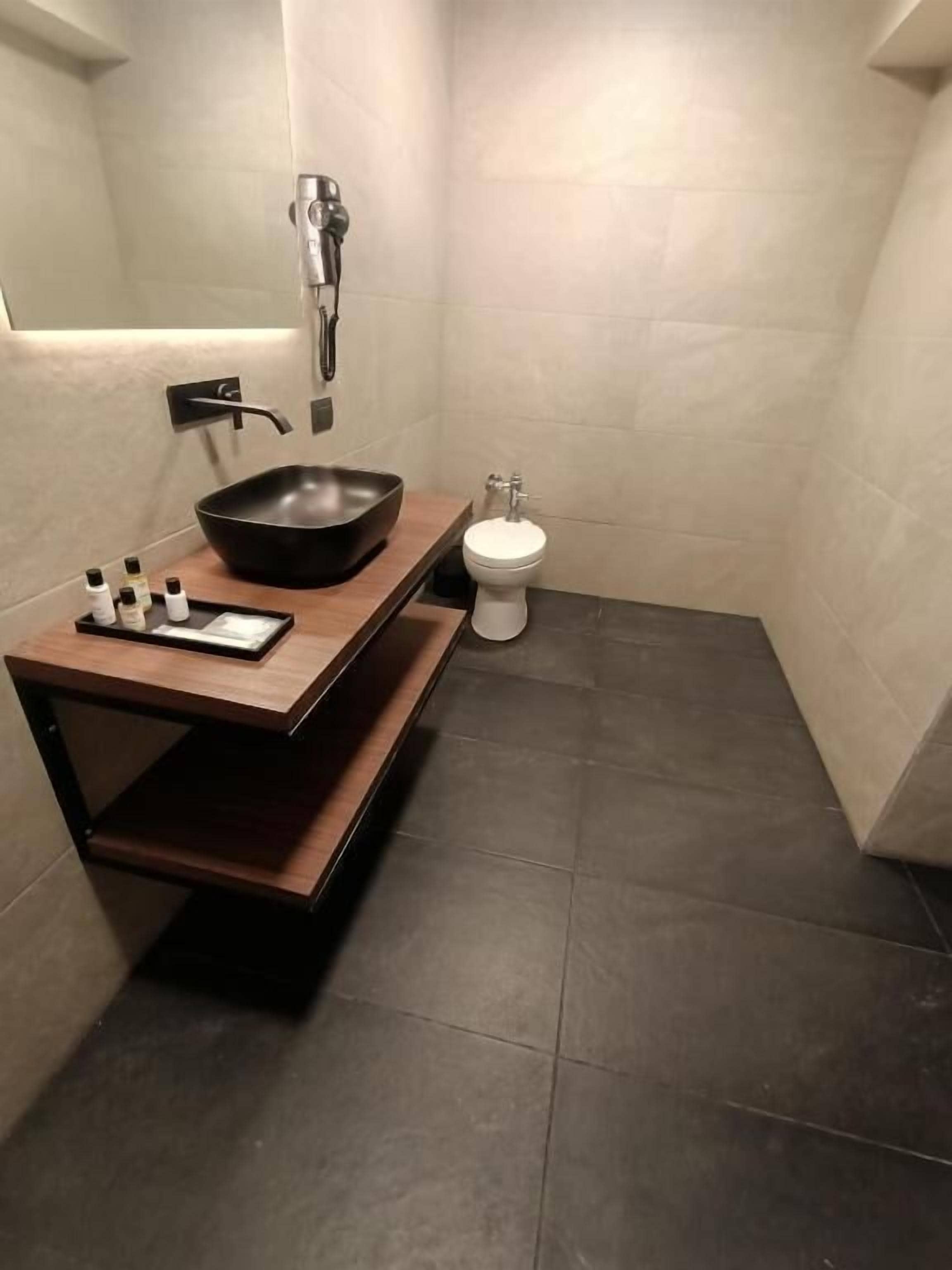 Un baño moderno con un lavamanos tipo cuenco negro, un inodoro blanco y un mueble de tocador de madera.