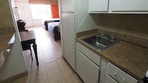A compact kitchen with a granite countertop, a stainless steel sink, and white cabinets. - White Marlin Inn (Virginia Beach)