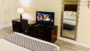 A hotel room with a TV on a desk, a bed with a checkered bedspread, a large mirror, and a lamp. - White Marlin Inn (Virginia Beach)