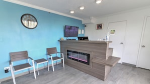 A reception area with a flat-screen TV, a fireplace, and two chairs. - White Marlin Inn (Virginia Beach)