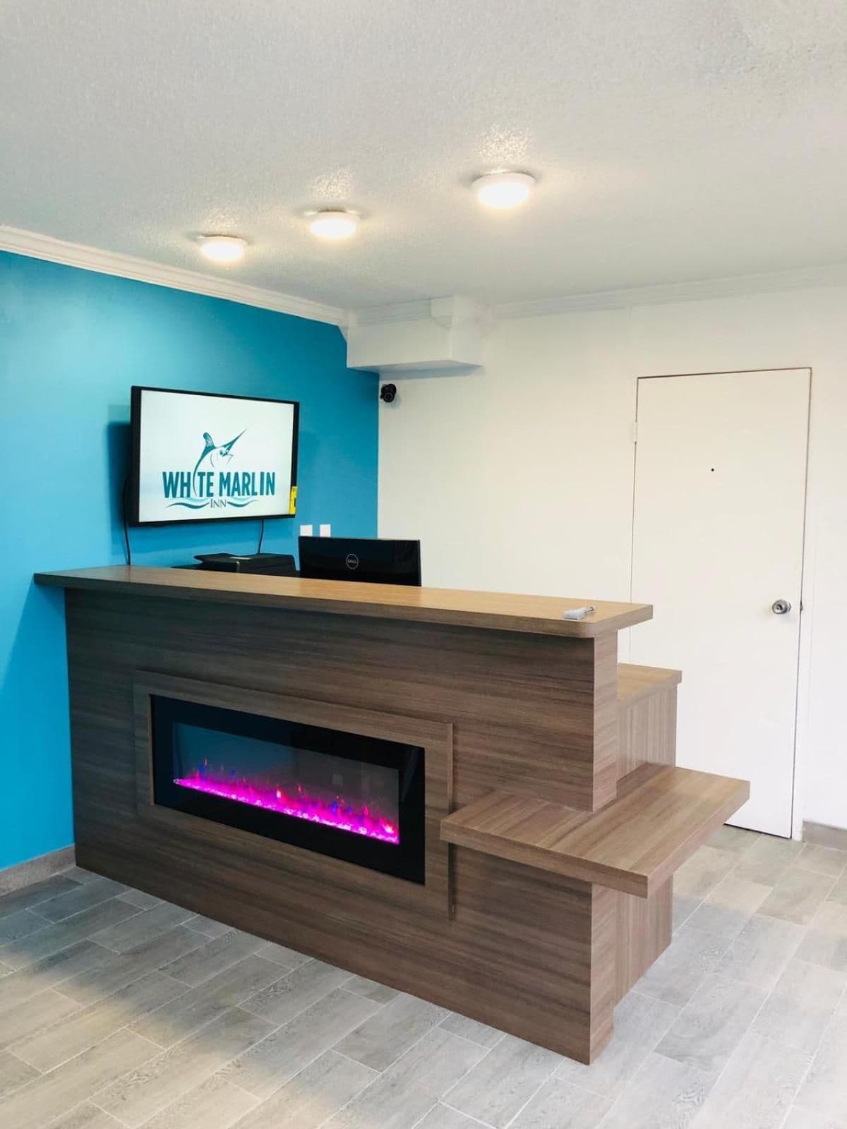 Una recepción con una televisión de pantalla plana mostrando el logotipo del White Marlin Inn, una chimenea empotrada y una escalera que lleva a un nivel superior.