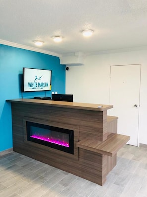 A reception desk with a flat-screen TV displaying the White Marlin Inn logo, a built-in fireplace, and a staircase leading to an upper level.