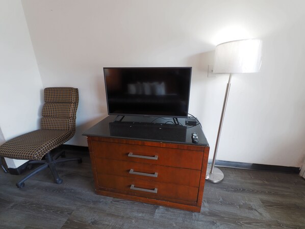 A room with a flat-screen TV on a wooden dresser, a chair, and a floor lamp.