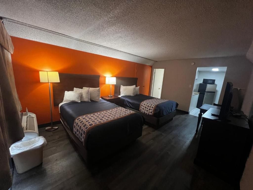 Quarto de hotel com duas camas, uma escrivaninha, uma cadeira, televisão e banheiro.