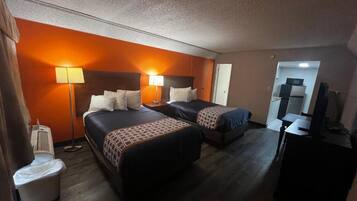 Quarto de hotel com duas camas, uma escrivaninha, uma cadeira, televisão e banheiro.