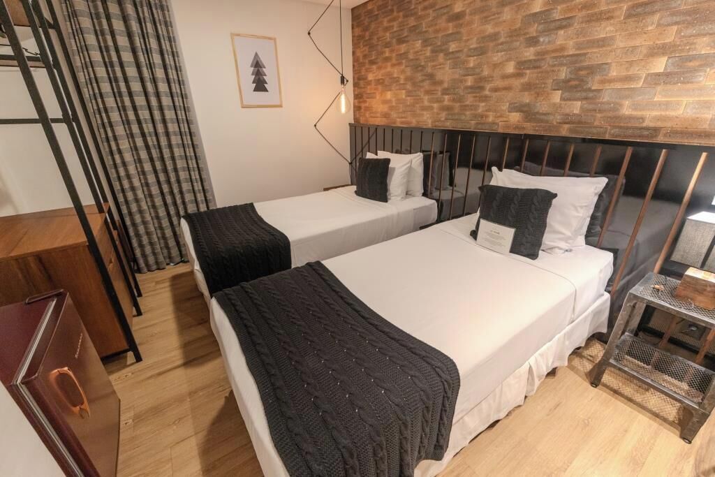 A hotel room with two beds, a wooden headboard, a metal lamp, and a small table.