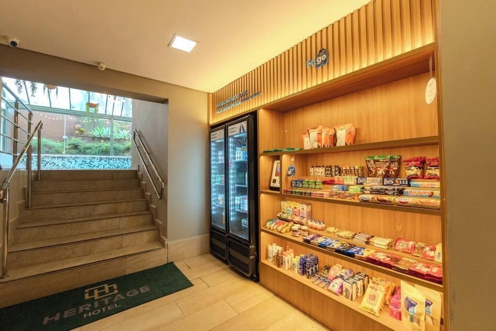 Vestíbulo de hotel con una escalera, un expositor refrigerado y estantes llenos de aperitivos.