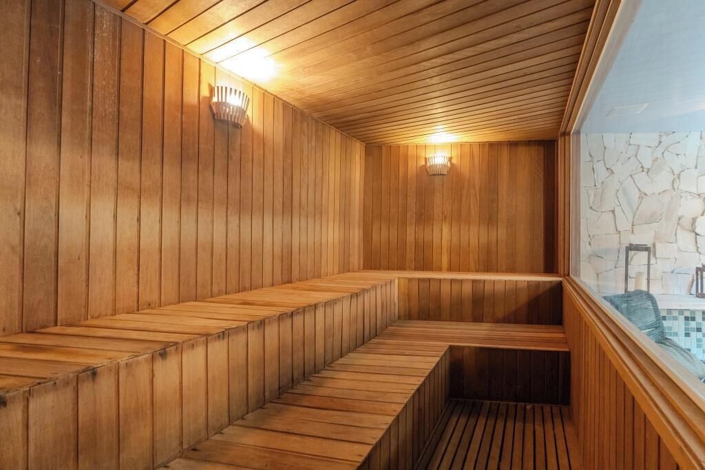 Un sauna avec des murs et des bancs en bois, un mur de pierre présentant un motif de fissures et une fenêtre offrant une vue dégagée.