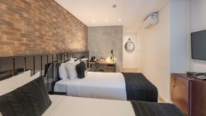 A hotel room with two beds, a desk, a chair, a TV, and a brick wall.