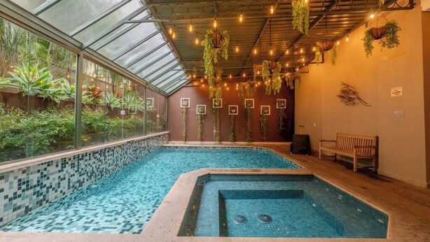 An indoor swimming pool with a glass ceiling, surrounded by potted plants and hanging greenery.