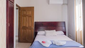 Ein Hotelzimmer mit Holztür, einem Bett mit weißer Bettwäsche und einer Klimaanlage an der Wand.