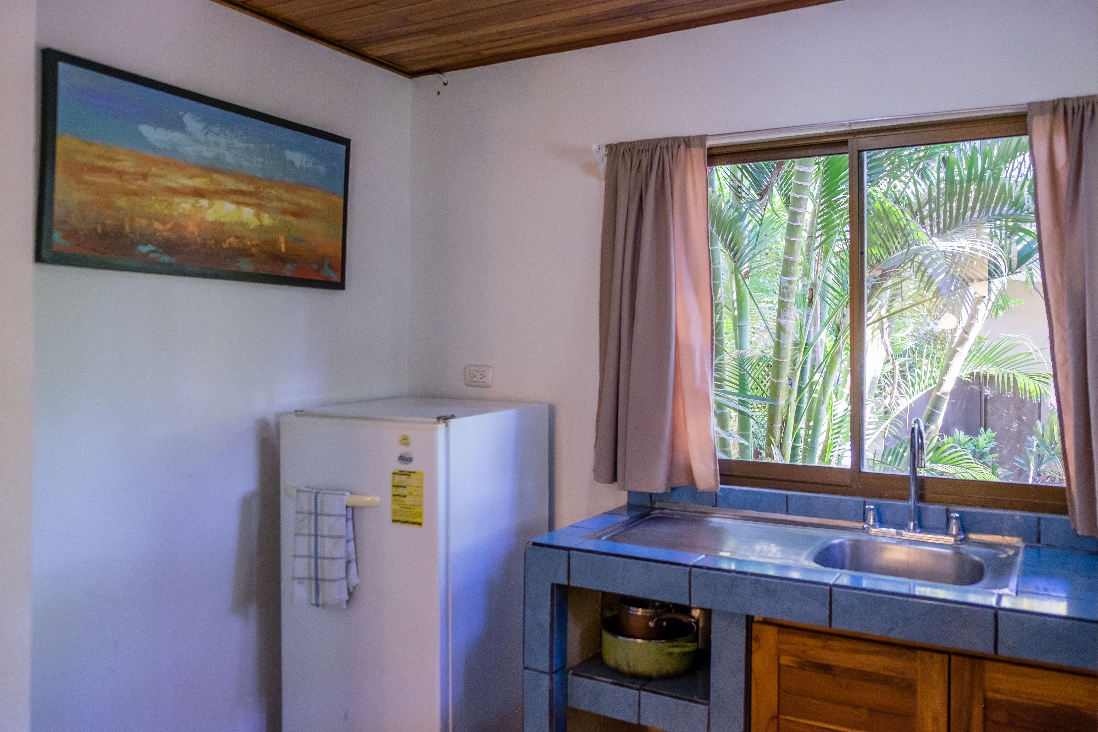A compact kitchen with a refrigerator, a sink, and a window with curtains.