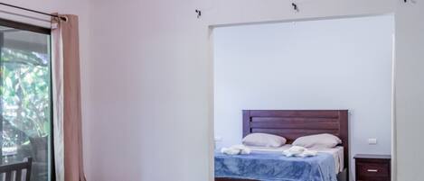 Un dormitorio con dos camas individuales, un ventilador de techo de madera, un espejo grande y un adorno decorativo en la pared.