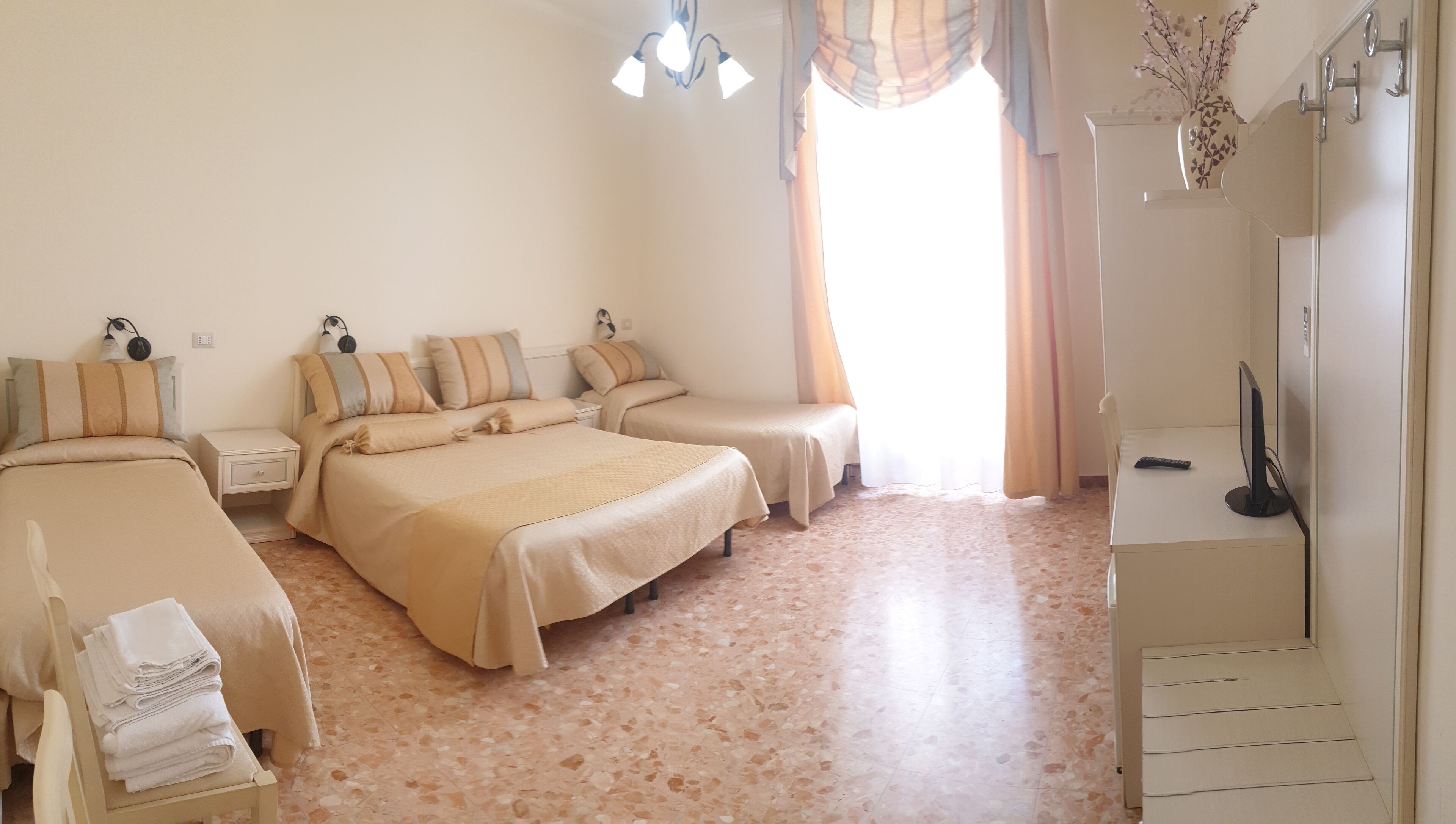 Una habitación de hotel con tres camas, un escritorio, una silla, un televisor y un baño.