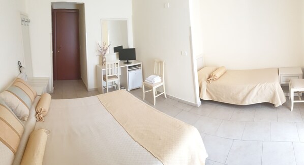 A hotel room with a large bed, a desk with a computer, a chair, and a small table. - RS San Sebastiano Holidays (Acireale)
