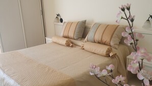 Een net opgemaakt bed met een geborduurde spreideken, twee kussens en een nachtkastje met een lamp.