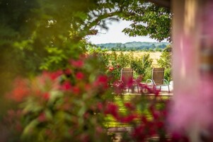Vista a un jardín con dos sillas y una mesa, rodeado de follaje y flores.
