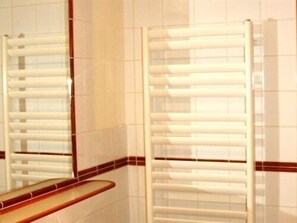 Un baño con paredes de azulejos blancos, encimera de madera y toallero blanco.