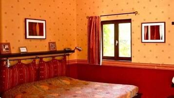 A room with a bed, two windows with curtains, a shelf with items, and a patterned wall.
