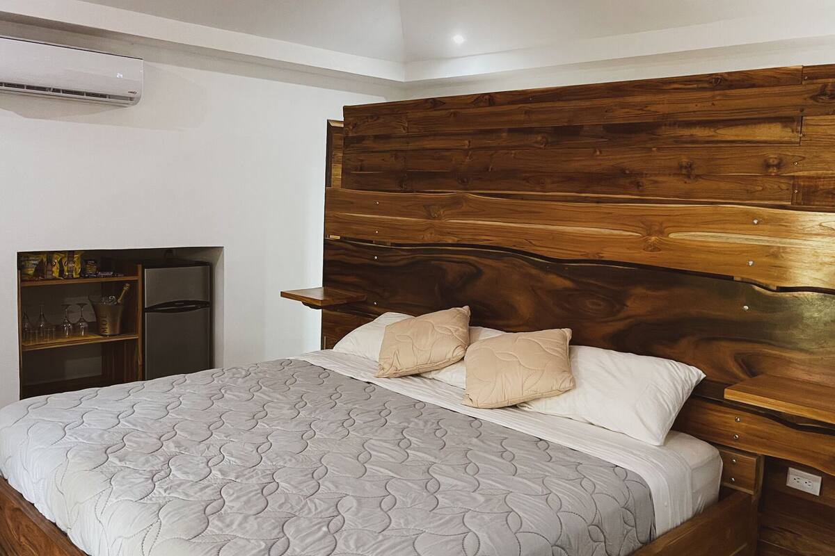 Een slaapkamer met een houten hoofdbord, een bed met een geborduurde matras en een inbouwkast met wijnrek.