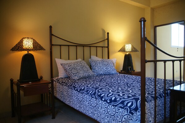 A bedroom with a four-poster bed, two bedside lamps, and a wooden nightstand. - Corail Suites (Petionville)