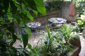 An outdoor patio area with round tables and chairs, surrounded by lush greenery and plants. - Corail Suites (Petionville)