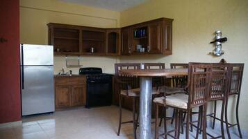 A kitchen with wooden cabinets, a stainless steel refrigerator, a stove, and a dining table with chairs.
