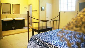 A bedroom with a bed, a window, and a bathroom with two sinks and mirrors. - Corail Suites (Petionville)