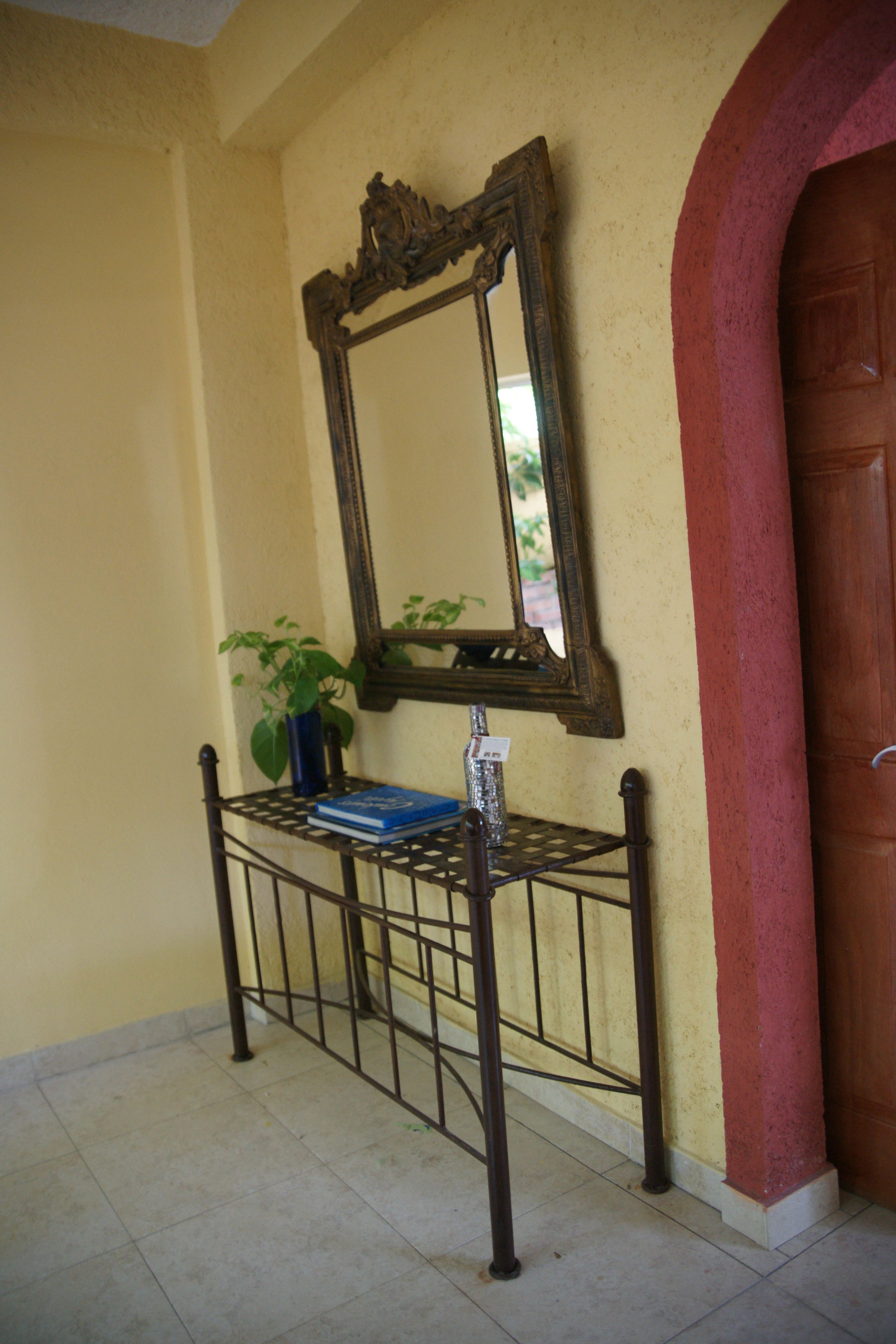 Un couloir avec un banc en métal, un miroir, une plante en pot et une porte en bois.