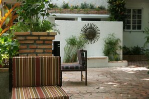 A patio area with a striped sofa and a chair, a brick planter with greenery, and a decorative wall with a sun motif. - Corail Suites (Petionville)