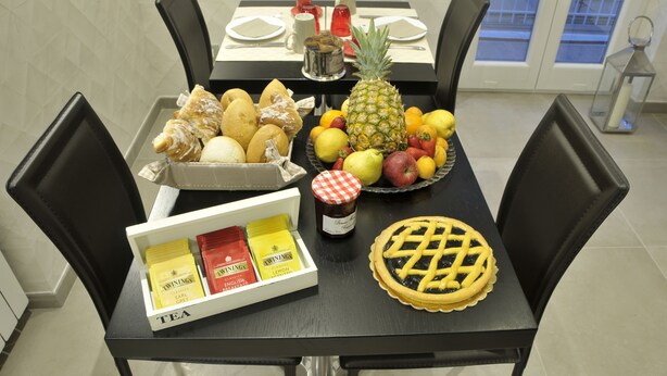 Uma mesa de jantar posta com uma variedade de frutas, doces e torta, além de uma caixa de chá e um pote de geleia.