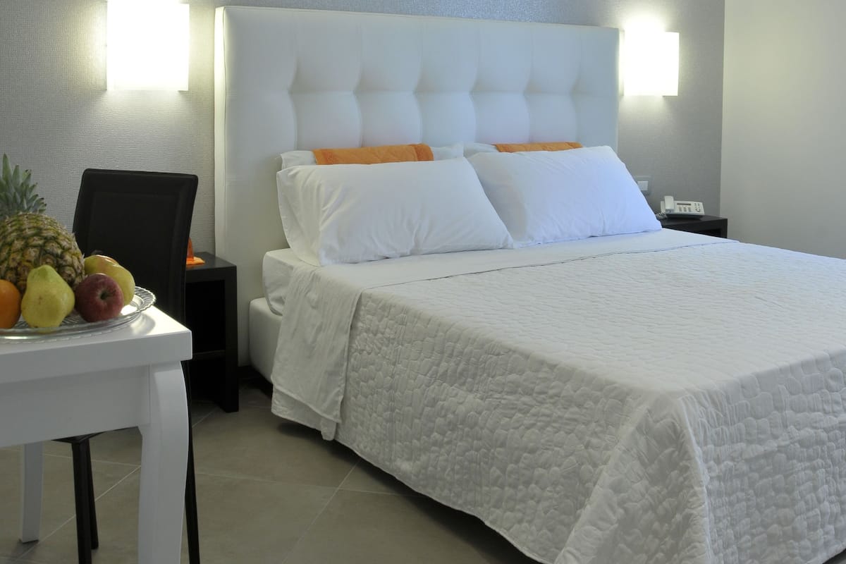 A hotel room with a large bed, white bedding, a small table with fruit, and two wall-mounted lights.