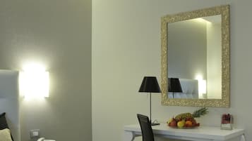 Quarto de hotel com cama, escrivaninha, cadeira, abajur, espelho e uma cesta de frutas.