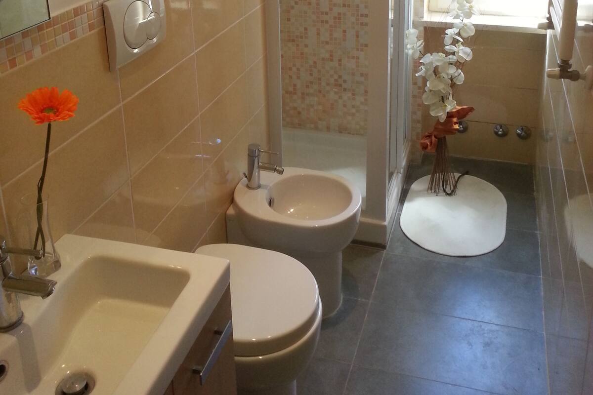 A bathroom with a sink, toilet, and shower. There is a towel rack with towels, a mirror, and a window.