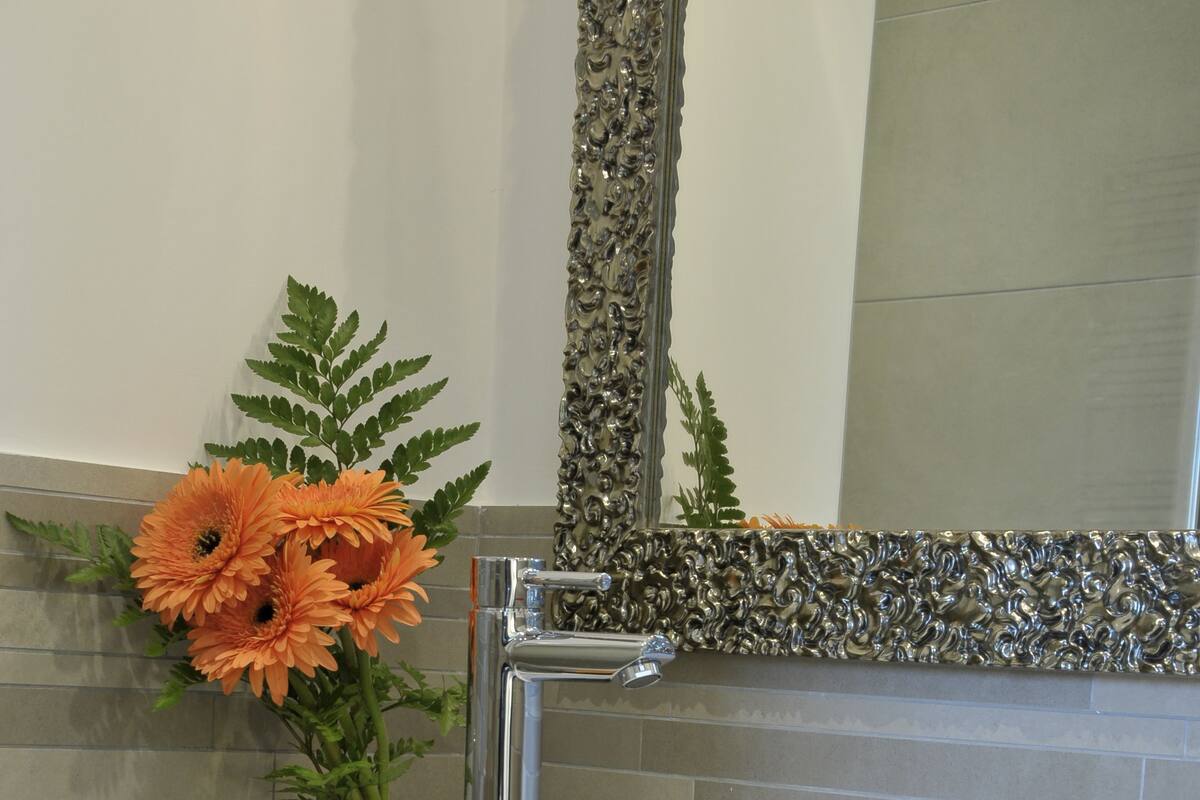 A bathroom with a white sink, a mirror with a decorative frame, and a vase with orange flowers.