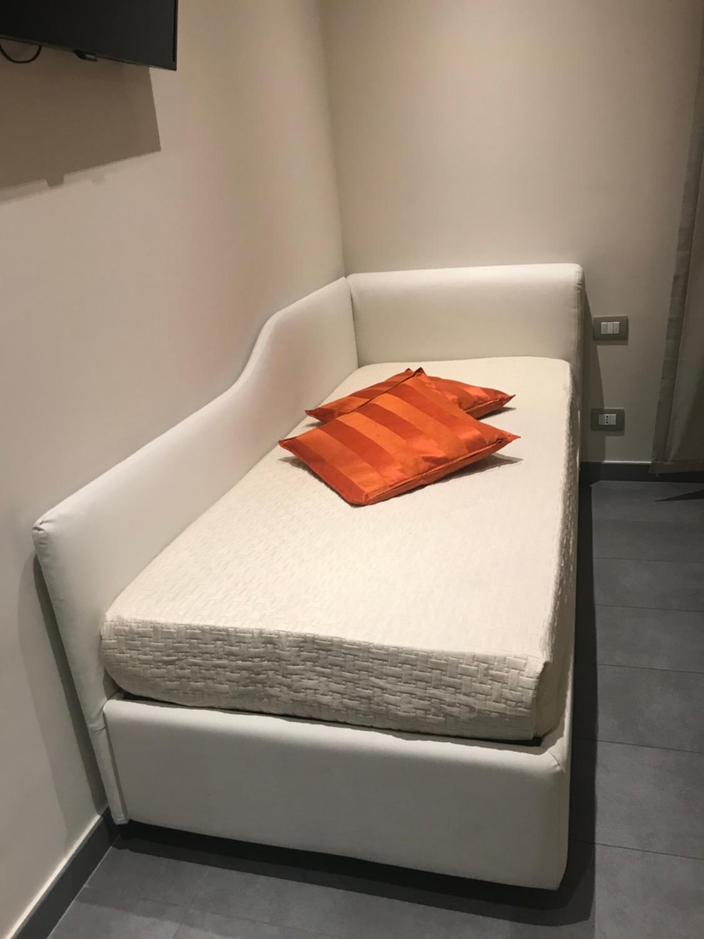 Un sofá pequeño blanco en forma de L, con funda texturizada blanca y dos almohadas naranjas.