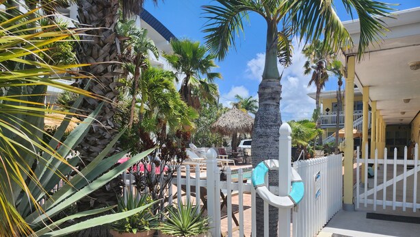 A tropical resort with a white fence, potted plants, and a palm tree. - Silver Sands Motel (Clearwater Beach)