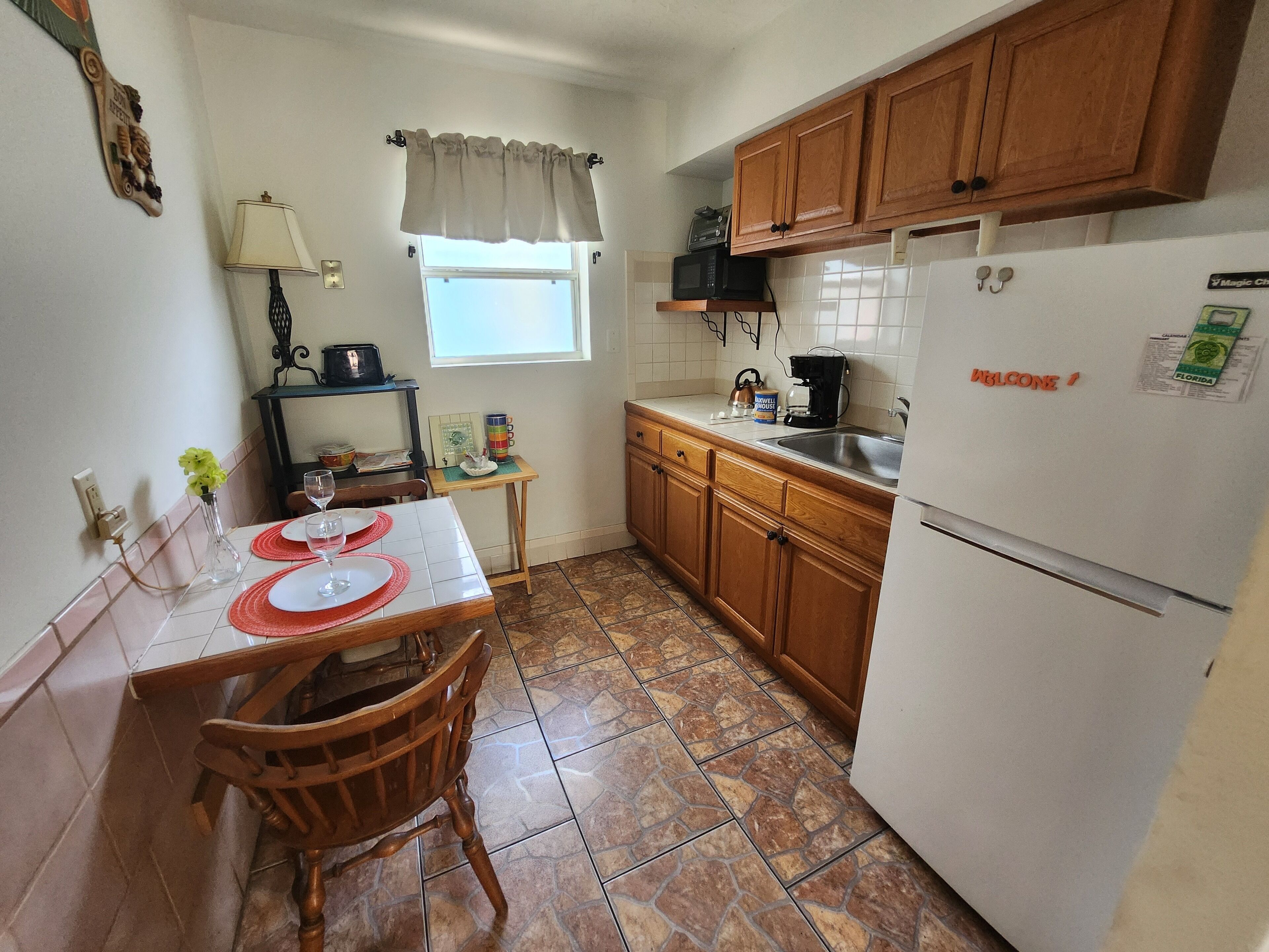 A compact kitchen with wooden cabinets, a refrigerator, a microwave, and a dining table with chairs.