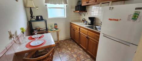 A compact kitchen with wooden cabinets, a refrigerator, a microwave, and a dining table with chairs.