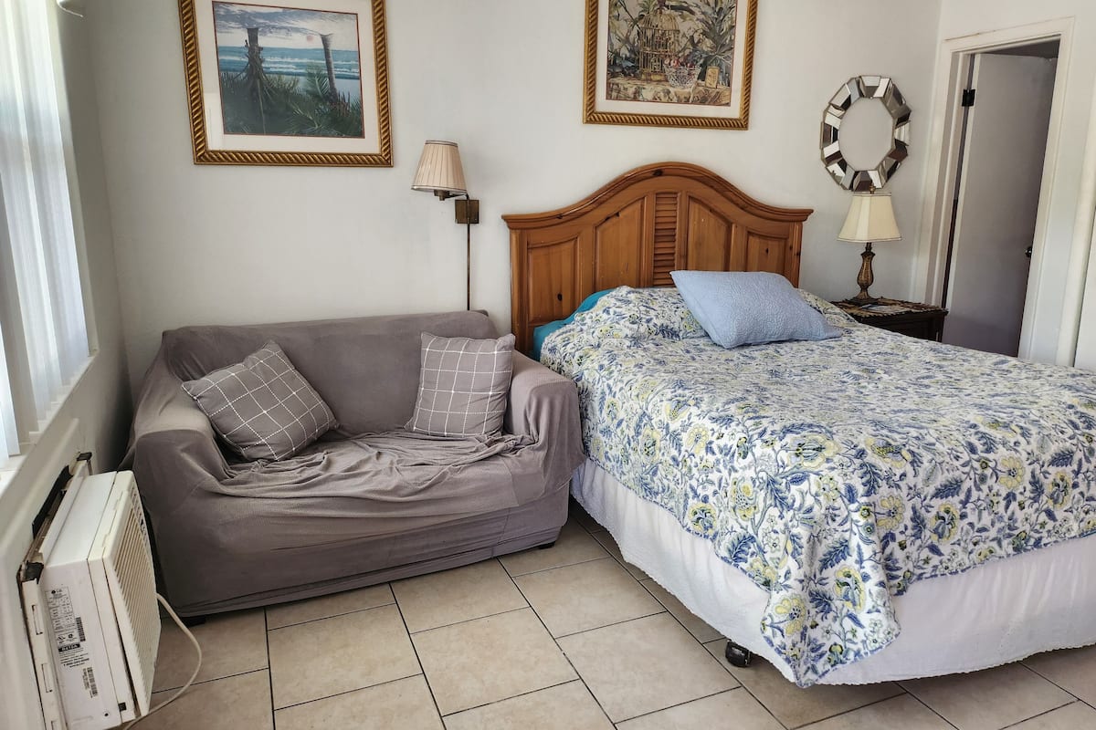 Une chambre à coucher avec un lit, un canapé, deux tableaux encadrés, une lampe et un radiateur.