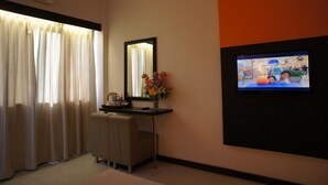 A hotel room with a desk, a mirror, a TV mounted on the wall, and a window with curtains. - Meldrum Hotel (Johor Bahru)