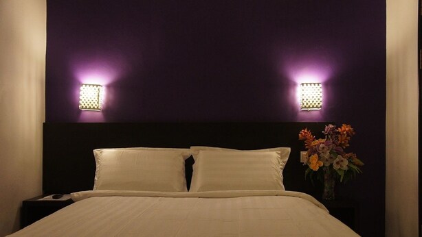 A neatly made bed with white linens, a dark headboard, and two wall-mounted light fixtures on either side. - Meldrum Hotel (Johor Bahru)