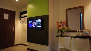 A hotel reception area with a television mounted on the wall, a mirror above the counter, and a vase of flowers. There are two white chairs in front of the counter. - Meldrum Hotel (Johor Bahru)