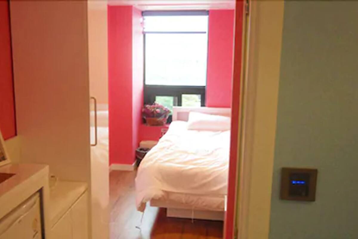 Un pasillo estrecho que conduce a un dormitorio con una cama, una mesita de noche y un ventanal.