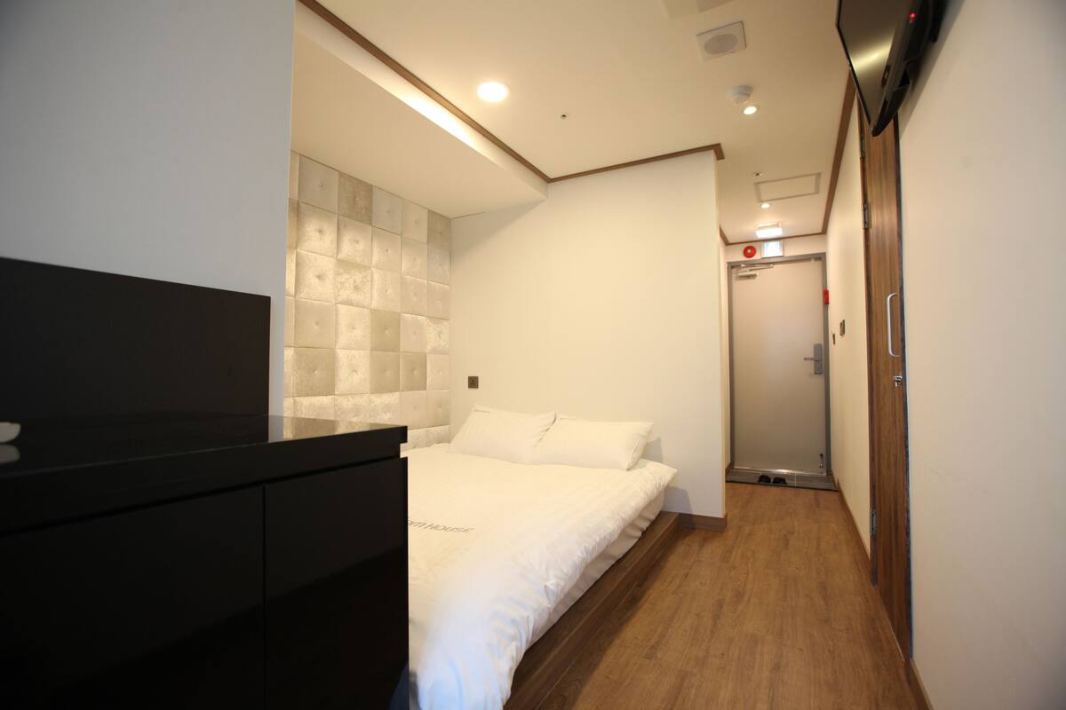 Una habitación de hotel moderna con una cama, piso de madera, un aparador negro y un televisor montado en la pared.