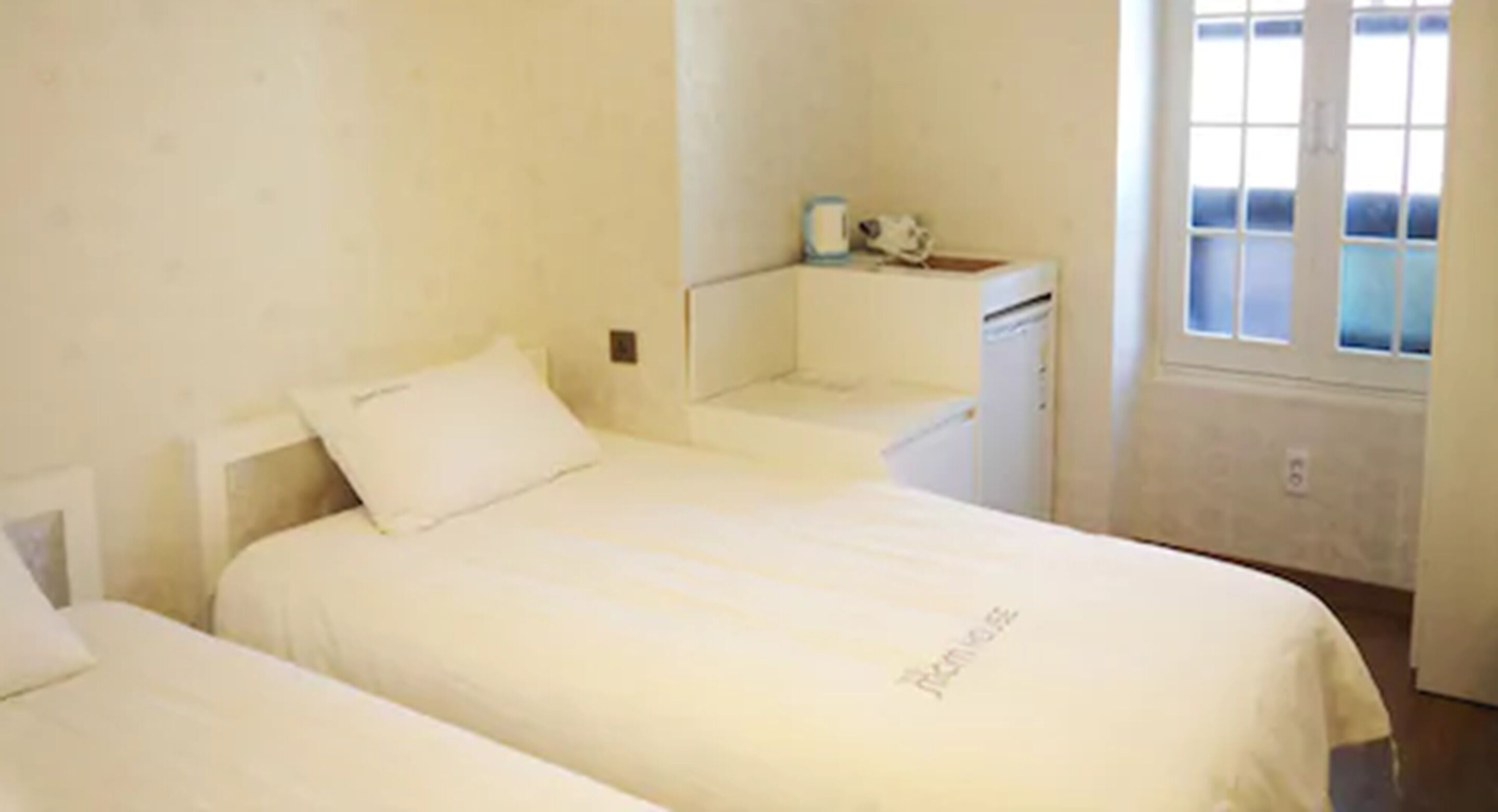 A small, clean room with two beds, a small desk, and a window.