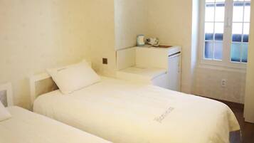 A small, clean room with two beds, a small desk, and a window.